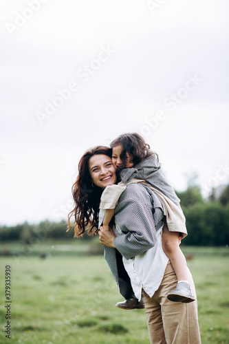 Stylish mother and daughter have fun outdoors in a field with green grass by the river when it rains