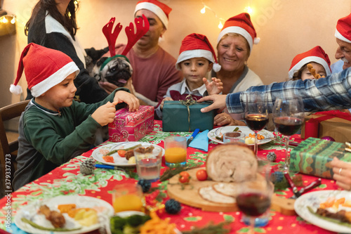 Happy family having Christmas dinner at home - Focus on right woman hand on green box present
