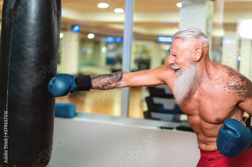 Senior hipster boxer hitting a huge punching bag at a boxing gym studio - Mature bearded man boxing and training - Fitness sport and healthy lifestyle -  Focus on face photo