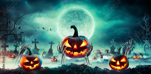 Jack O’ Lantern On Skeleton Arms In Graveyard At Night - Halloween With Full Moon