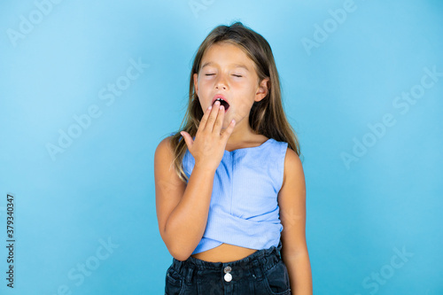 Young beautiful child girl over isolated blue background bored yawning tired covering mouth with hand. Restless and sleepiness.