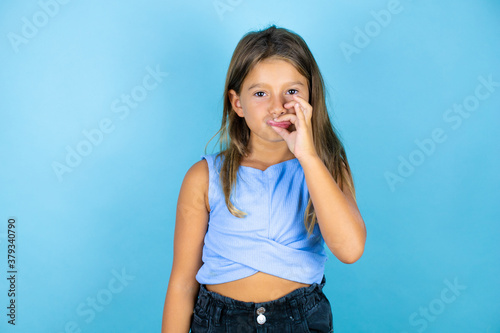 Young beautiful child girl over isolated blue background mouth and lips shut as zip with fingers. Secret and silent, taboo talking photo
