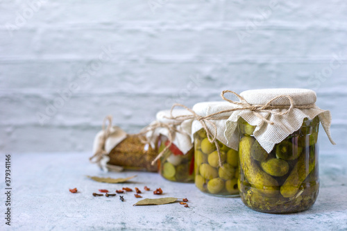 Jars with pickled cucumbers, olives and fermented vegetables salad on white wall background