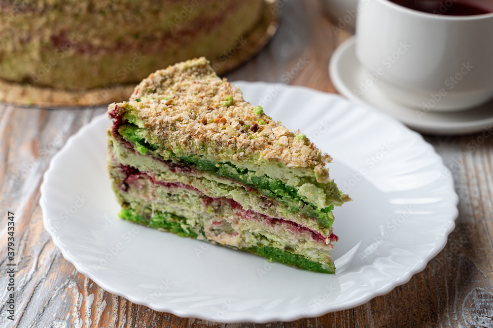 Slice of green pistachio sponge on a wooden table, with a whole torte on background Slice of green pistachio sponge on a wooden table, with a whole torte on background