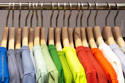 Multicolored shirts and sweatshirts hang on wooden hangers close-up.
