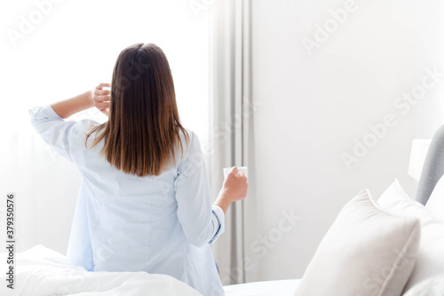 Morning at home. Woman drinking coffee in bed by window. Girl enjoying tea and relaxation in cozy bedroom. White background and copy space.