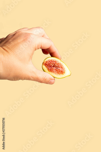 Hand holding half fig on yellow plain background