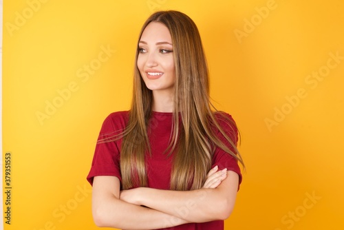 Portrait of dreamy rest relaxed Beautiful Young beautiful caucasian girl wearing red t-shirt over isolated yellow background crossing arms, looks good