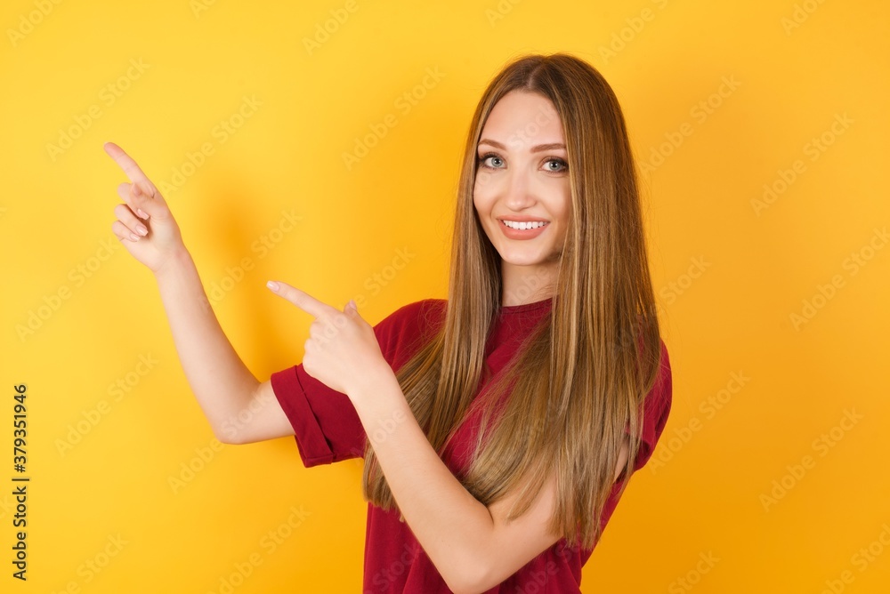 Beautiful Young beautiful caucasian girl wearing red t-shirt over isolated yellow background indicating with forefinger empty space showing best low prices
