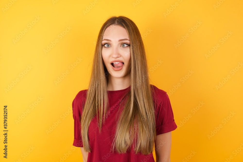 Beautiful Young beautiful caucasian girl wearing red t-shirt over isolated yellow background showing grimace face crossing her eyes and showing tongue . Being funny and crazy Beautiful Young beautiful caucasian girl wearing red t-shirt over isolated yellow background showing grimace face crossing her eyes and showing tongue . Being funny and crazy