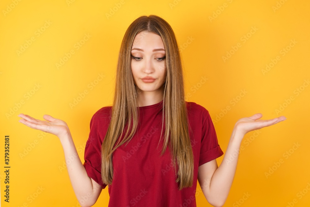 Hesitant Beautiful Young beautiful caucasian girl wearing red t-shirt over isolated yellow background shrugs shoulders, looks uncertain and confused. Have no answer Hesitant Beautiful Young beautiful caucasian girl wearing red t-shirt over isolated yellow background shrugs shoulders, looks uncertain and confused. Have no answer