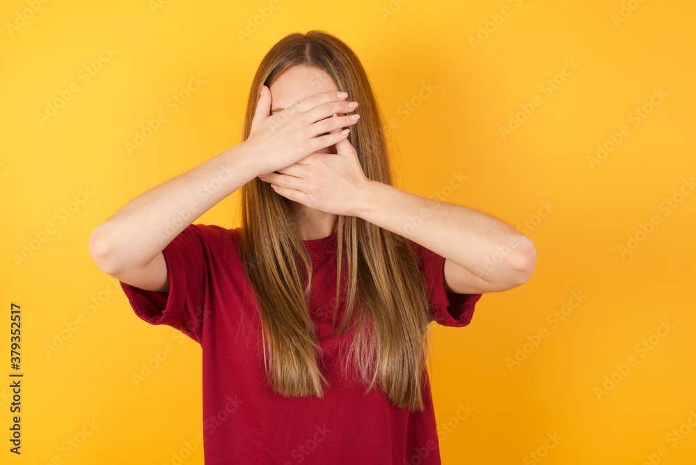 Beautiful Young beautiful caucasian girl wearing red t-shirt over isolated yellow background Covering eyes and mouth with hands, surprised and shocked. Hiding emotions. Beautiful Young beautiful caucasian girl wearing red t-shirt over isolated yellow background Covering eyes and mouth with hands, surprised and shocked. Hiding emotions.