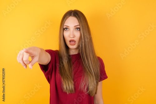 Beautiful Young beautiful caucasian girl wearing red t-shirt over isolated yellow background Pointing with finger surprised ahead, open mouth amazed expression, something on the front.