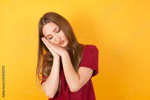 Beautiful Young beautiful caucasian girl wearing red t-shirt over isolated yellow background sleeping tired dreaming and posing with hands together while smiling with closed eyes.