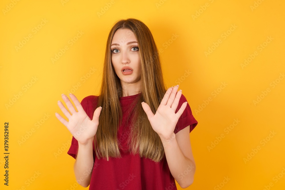 Beautiful Young beautiful caucasian girl wearing red t-shirt over isolated yellow wall Moving away hands palms showing refusal and denial with afraid and disgusting expression. Stop and forbidden. Beautiful Young beautiful caucasian girl wearing red t-shirt over isolated yellow wall Moving away hands palms showing refusal and denial with afraid and disgusting expression. Stop and forbidden.