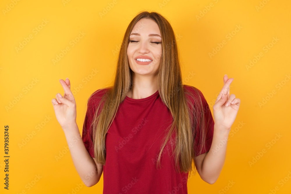 Beautiful Young beautiful caucasian girl wearing red t-shirt over isolated yellow background gesturing finger crossed smiling with hope and eyes closed. Luck and superstitious concept. Beautiful Young beautiful caucasian girl wearing red t-shirt over isolated yellow background gesturing finger crossed smiling with hope and eyes closed. Luck and superstitious concept.