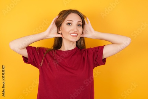 Beautiful Young beautiful caucasian girl wearing red t-shirt over isolated yellow background Trying to hear both hands on ear gesture, curious for gossip. Hearing problem, deaf