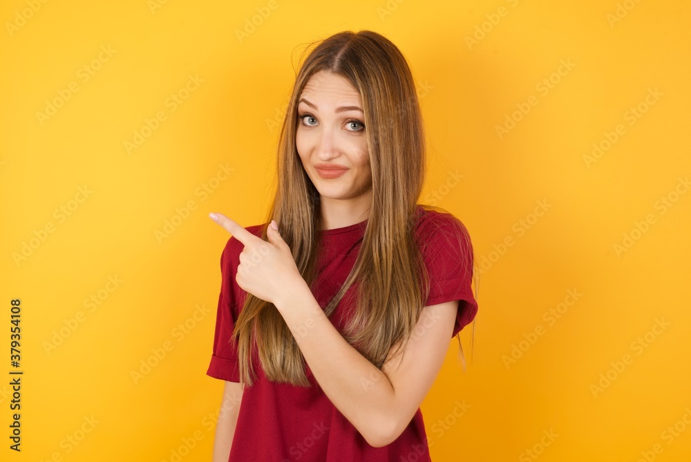 Beautiful Young beautiful caucasian girl wearing red t-shirt over isolated yellow background Pointing aside worried and nervous with forefinger, concern and surprise concept. Beautiful Young beautiful caucasian girl wearing red t-shirt over isolated yellow background Pointing aside worried and nervous with forefinger, concern and surprise concept.