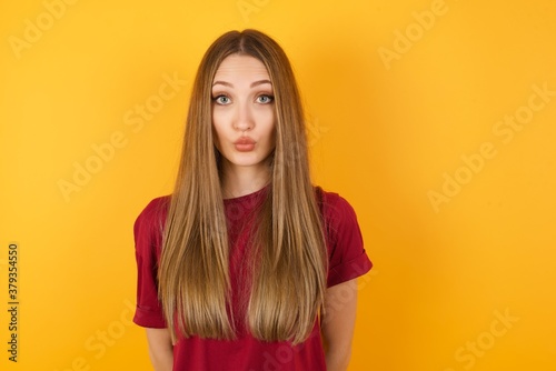 Shot of pleasant looking Beautiful Young beautiful caucasian girl wearing red t-shirt  pouts lips, looks with green eyes at camera,  has fun with boyfriend, Human facial expressions © Roquillo