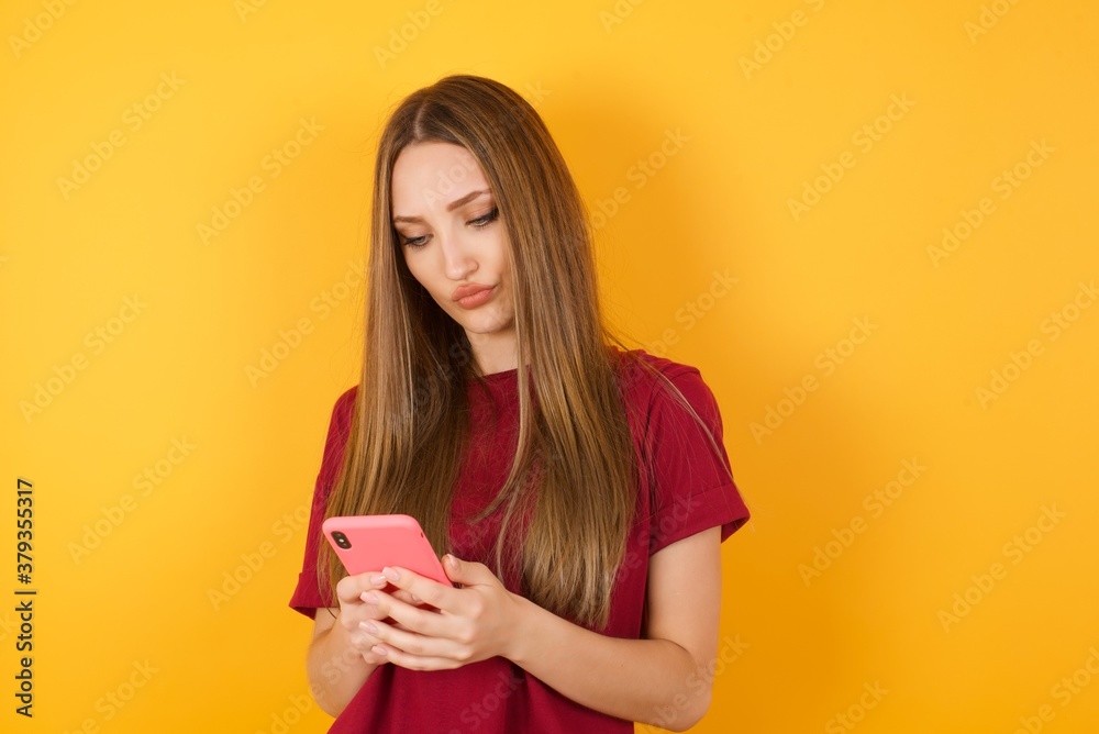 Crazy Beautiful Young beautiful caucasian girl wearing red t-shirt over isolated yellow wall use cell phone reads incredible news on social media information stare, screams wow omg wear stylish outfit