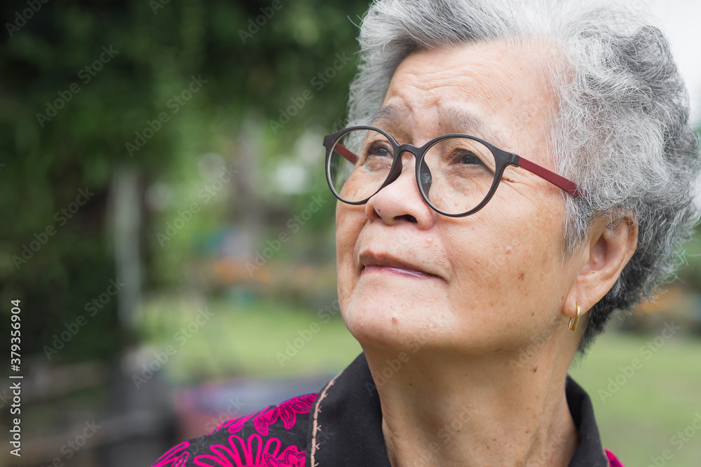 Senior Asian woman looking up while standing in a garden Senior Asian woman looking up while standing in a garden