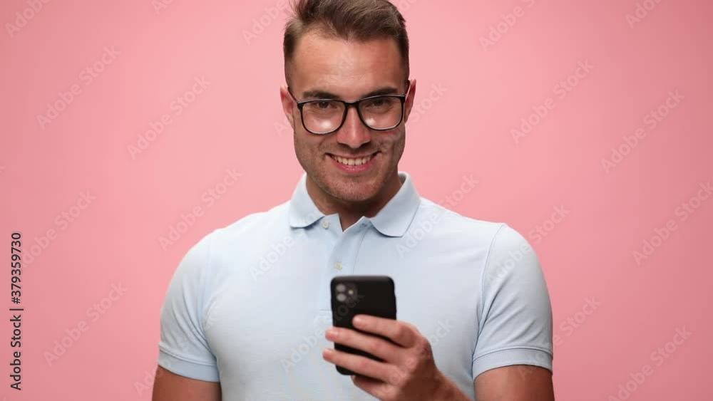 young casual man looking at his phone and texting, smiling against pink background young casual man looking at his phone and texting, smiling against pink background