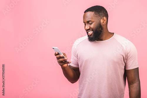 Portrait of handsome excited cheerful joyful delightful african american guy wearing casual sending and getting messages to his lover isolated against pink background. Using phone. © denis_vermenko