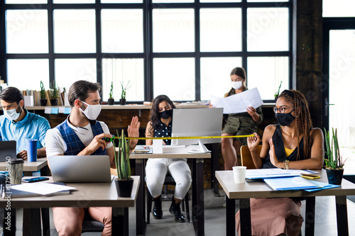 Business people with face masks in office, coronavirus and safe distance concept.