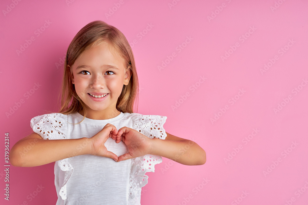 friendly kind girl shows heart made from hands at camera, loves everyone. isolated pink background friendly kind girl shows heart made from hands at camera, loves everyone. isolated pink background