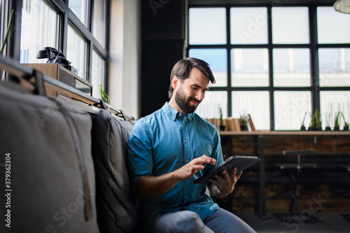 Portrait of young businessman with tablet indoors in office, looking at camera.