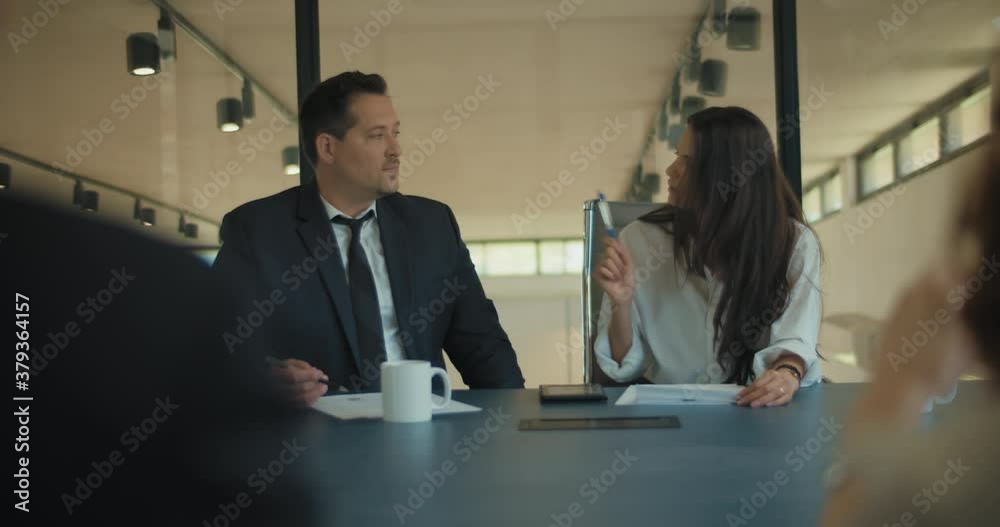 Medium shot of two business people discuss project ideas with their colleagues in the office meeting room. Slow motion. 