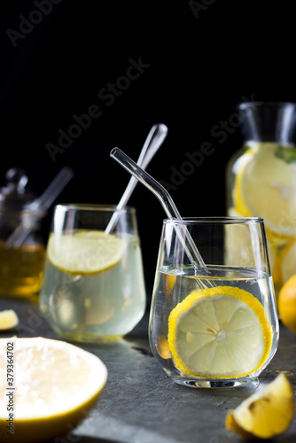 Two glasses of lemonade on a black background. Lemon slices and mint leaves float in the water and lie next to each other on the table