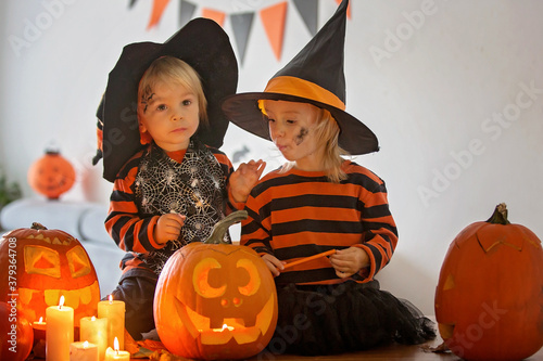 Children, toddler boy and girl, playing with carved pumpkin at home on Halloween, making magic potion