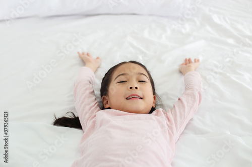 Happy asian little girl lying smile on white bed and raise one's hand.
