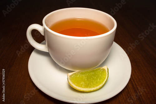 a cup of black tea on a saucer with a slice of lime on a dark brown wooden background
