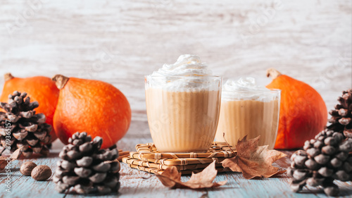 Pumpkin pie smoothie on worn wooden table with cedar cones and dry leaves. Autumn still life with pumpkin smoothie decorated with whipped cream closeup