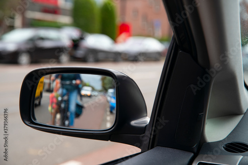 Blurred defocused photo. People on the bicycles in the city traffic. View in the side mirror of the car.