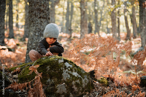 Little caucasian baby girl squatting in the forest among ferns © Manu Reyes