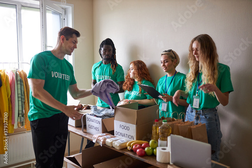 group of diverse people working in charitable foundation  happy caucasian and african volunteers looking at donation box  separating donations stuffs