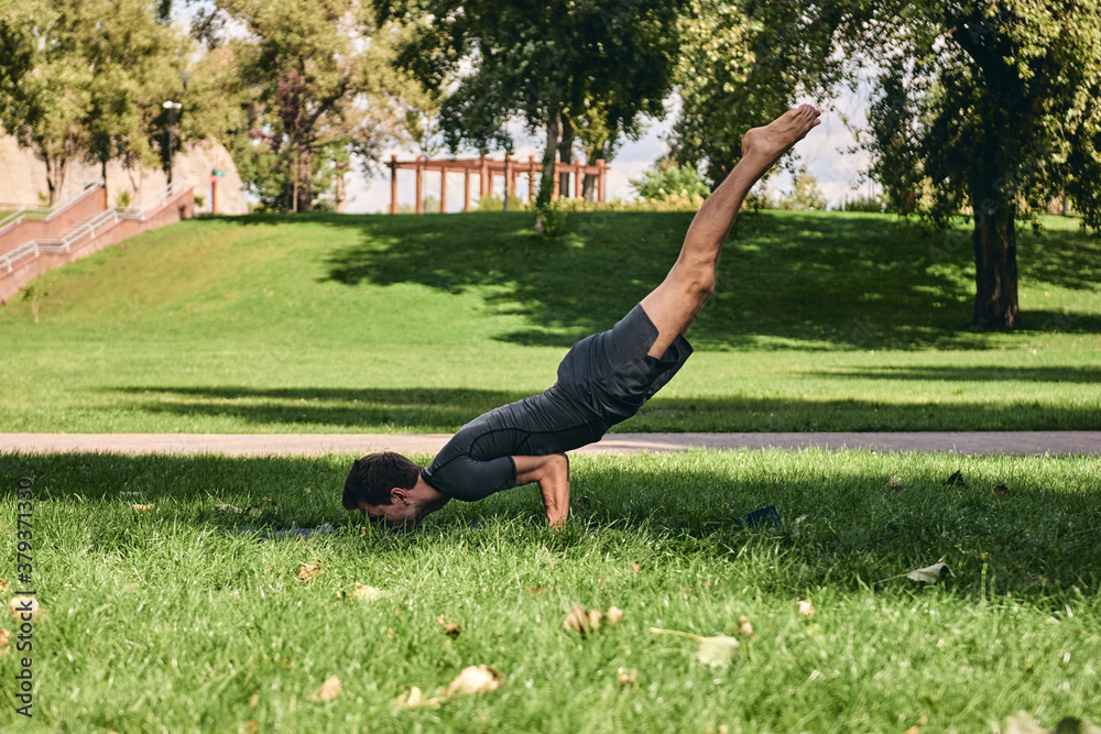 Young athletic man in sportswear doing yoga in the park. Practice asana outdoors. People exercising on green grass with yoga mat. Strong mature caucasian man in difficult peacock pose Young athletic man in sportswear doing yoga in the park. Practice asana outdoors. People exercising on green grass with yoga mat. Strong mature caucasian man in difficult peacock pose