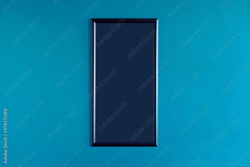 Black, blank frame hanging on the interior blue wall. Empty frame mock up. Black, blank frame hanging on the interior blue wall. Empty frame mock up.