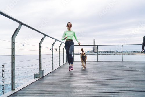 Cheerful sportswoman jogging with dog on embankment © BullRun