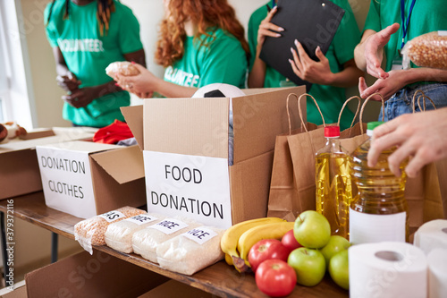 diverse volunteers collecting food and clothes donations in warehouse, multi-ethnic team of volunteers holding donations boxes in a large warehouse, they are putting clothes in boxes