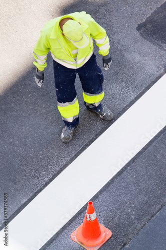 construction worker with reflective vest and helmet in road site painting white marks on ground