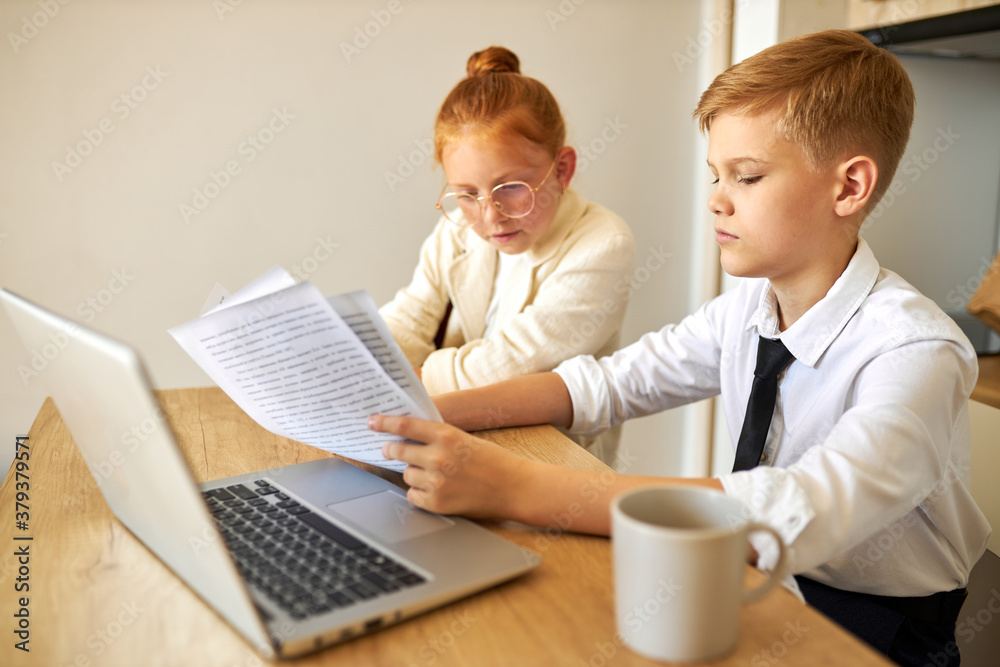 friendly kids couple behave themselves as adults, solve work problems together, look at laptop and documents, checking bills, making purchase online, freelance. children, people concept friendly kids couple behave themselves as adults, solve work problems together, look at laptop and documents, checking bills, making purchase online, freelance. children, people concept