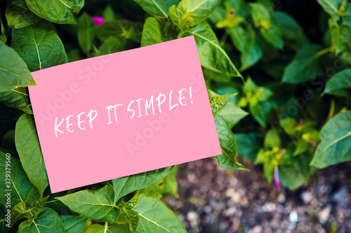 Keep it simple motivational quote written on pink paper on green garden and nature background. Peaceful, comfortable and simplified life concept. © Cagkan
