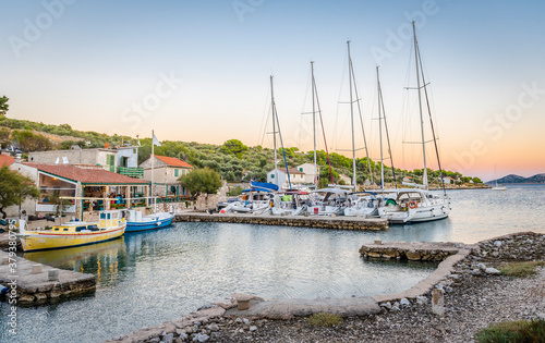 Yachts and wooden fishing boats in the bay of the Adriatic sea and dining people under a canopy in a fishing village in Lavsa, Croatia photo