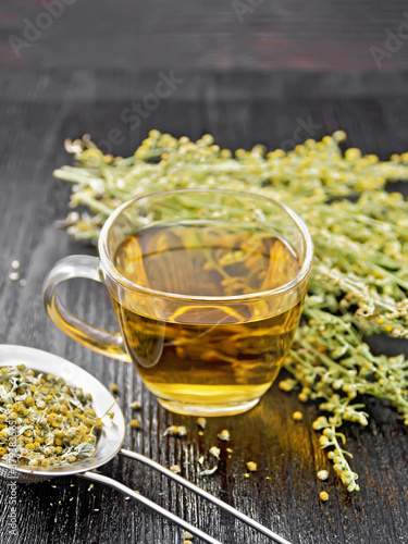Tea of gray wormwood in glass cup with strainer on black board