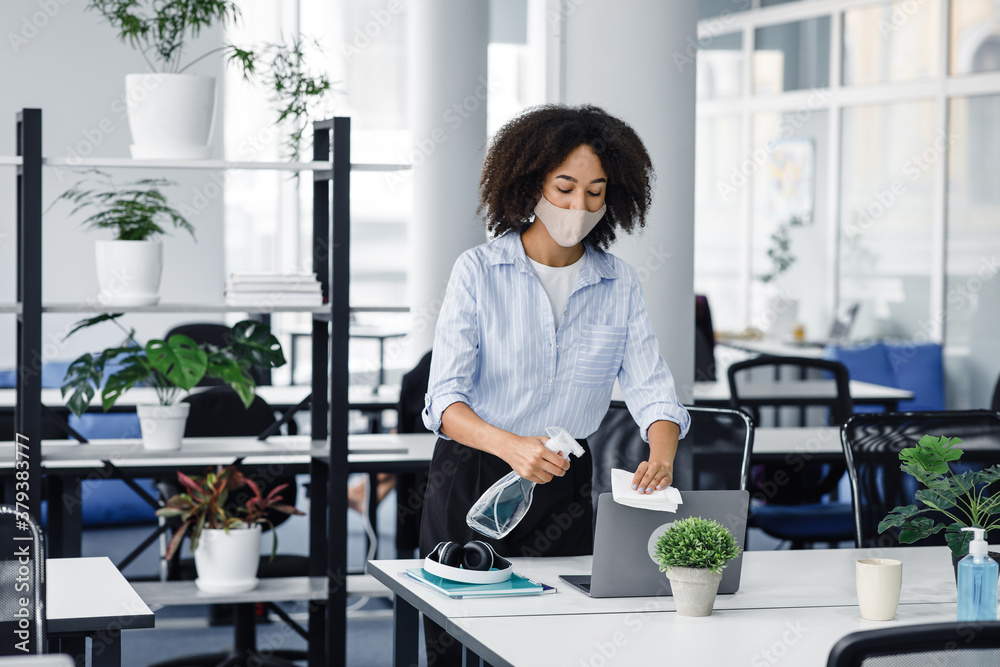 Prevention of coronavirus. African american millennial girl in protective mask disinfects laptop Prevention of coronavirus. African american millennial girl in protective mask disinfects laptop