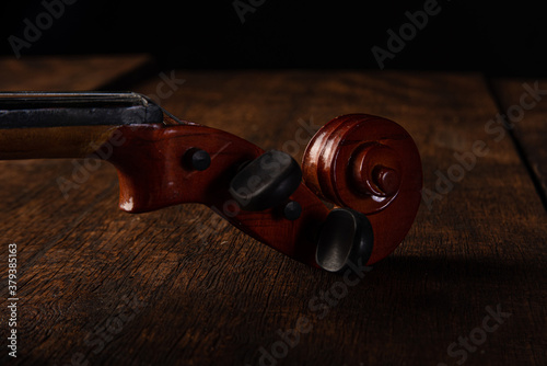 Details of an old and beautiful violin on a rustic wooden surface and black background, low key portrait, selective focus.